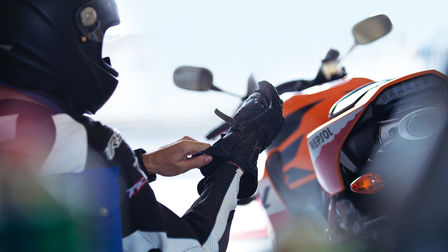 Pilote enfilant correctement son gant droit. Arri&egrave;re de la moto, &agrave; la droite du pilote.