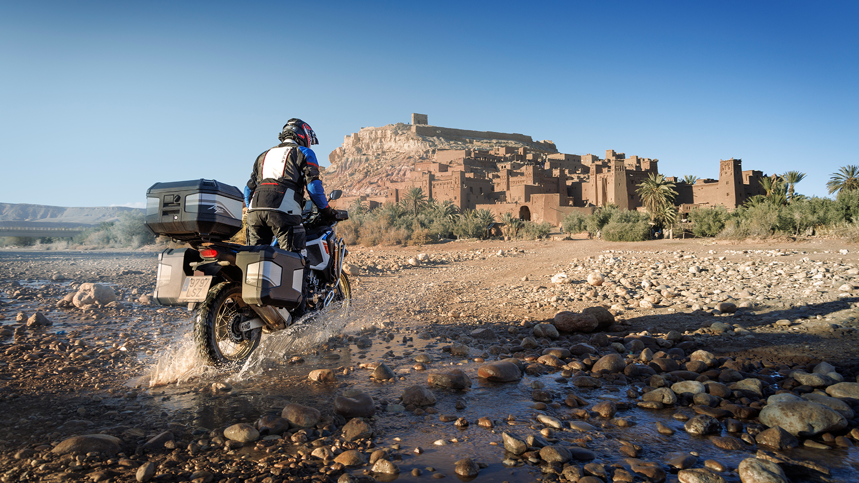 Motard sur CRF1100 ATAS dos à la route avec accessoires de randonnée.