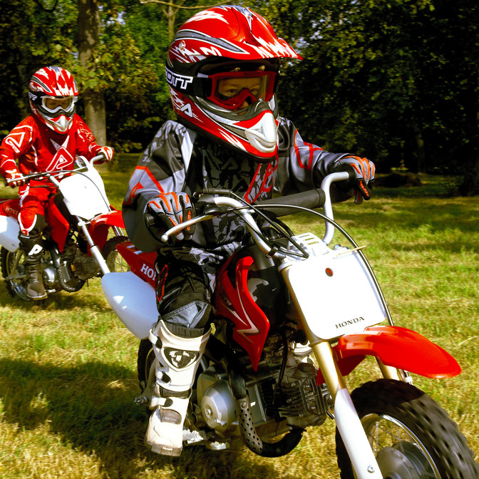 Vue de trois quarts latérale de 2 motos CRF50F avec conducteurs, pendant une course sur herbe. Vue de face