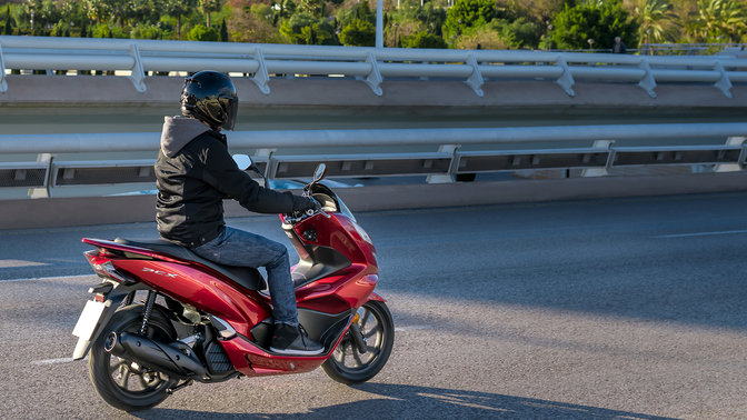 Vue lat&eacute;rale du scooter PCX125 avec pilote, dans une rue.