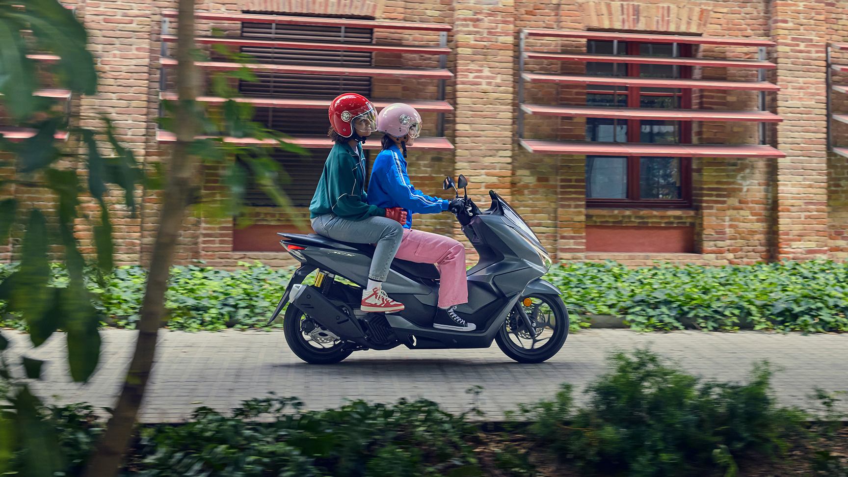 Plan latéral de mannequins à bord de la moto PCX125 en milieu urbain.