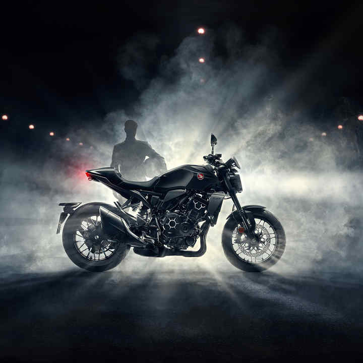 Coté droite du roadster Honda CB1000R Black Edition, noire, conducteur derrière la moto avec du brouillard la nuit