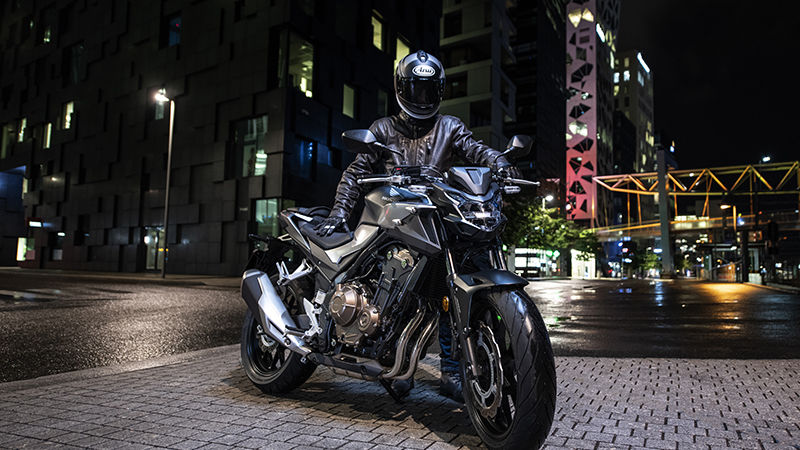 Vue de trois quarts avant droit de la CB500F, en stationnement dans un paysage urbain avec un pilote